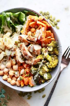 a white bowl filled with vegetables and chickpeas on top of a table next to a fork