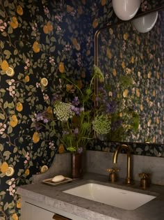 a bathroom sink sitting under a mirror next to a wall papered with floral designs