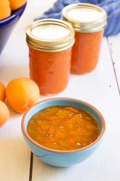 three jars of orange marmalade sit on a table next to tangerines