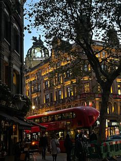 people are walking down the street in front of some tall buildings at night with lights on