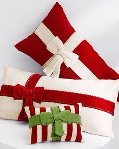 three red and white christmas pillows with bows on them, one has a green bow