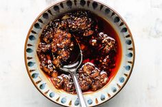 a bowl filled with meatballs and sauce on top of a white tablecloth next to a spoon