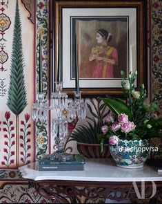 a painting on the wall above a table with wine glasses and flowers in front of it