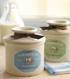 two jars sitting on top of a counter next to a bottle of milk and a cloth