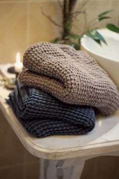 three folded sweaters sitting on top of a table next to a bowl and candle