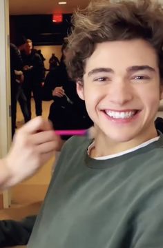 a young man smiles as he gets his hair cut by another person in the background