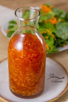 a glass bottle filled with liquid sitting on top of a plate next to a salad