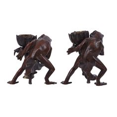 two bronze figurines of men carrying baskets on their backs, one holding a planter