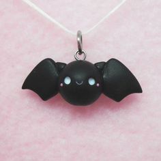 a black bat necklace with blue eyes on a pink background