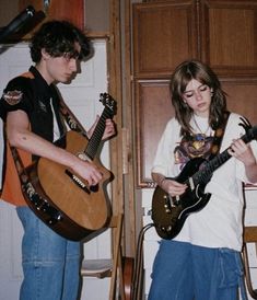 two young people playing guitars in a room