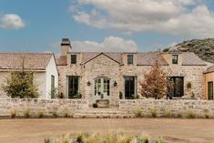 a stone house with green shutters on the front and side windows, surrounded by greenery