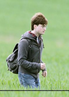 a young boy walking through the grass with a backpack