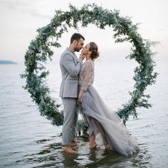 a newly married couple standing in the water holding each other's hands and kissing