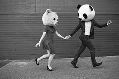 a man and woman walking down the street holding hands with a giant panda bear head