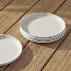 three white plates sitting on top of a wooden table next to each other and one is empty