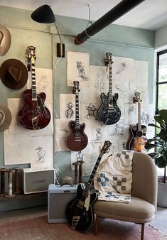 guitars are hanging on the wall next to a chair and guitar rack in a room