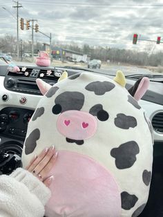 a woman is holding a cow pillow in her hand while she sits in the driver's seat