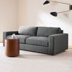 a grey couch sitting on top of a white rug in a living room next to a lamp