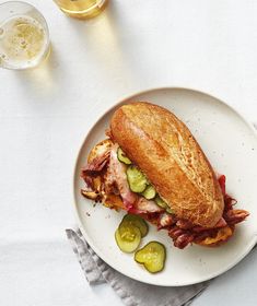 a sandwich on a plate with pickles next to two glasses of beer and napkins