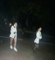 two women in white dresses are walking down the street at night with their cell phones up to their ears