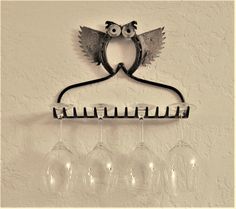 a wine glass rack with five glasses hanging from it's side and an owl on the top