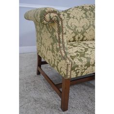 a green and beige patterned chair sitting on top of a carpeted floor next to a wall