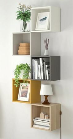 a shelf with books, plants and pictures on it in the corner of a room