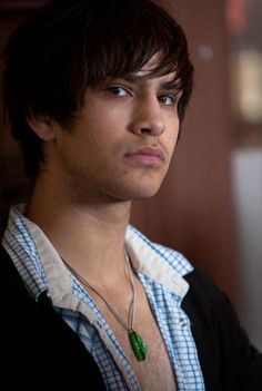 a close up of a person wearing a necklace and looking off to the side with a serious look on his face