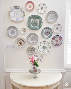 a vase with flowers sitting on top of a table next to plates hanging on the wall