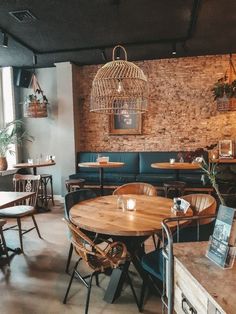 an empty restaurant with wooden tables and blue couches in front of a brick wall