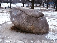 a large rock sitting in the middle of a snow covered park with benches and trees