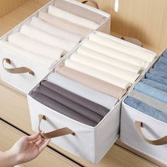 two white storage bins filled with folded towels and folded linens, one being held by a woman's hand