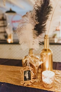 a table topped with a bottle and a vase filled with white feathers next to a candle