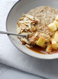 oatmeal with apples and nuts in a bowl on a white cloth next to a spoon