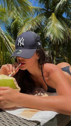 a woman laying on top of a table next to a green coconut and drinking from a straw