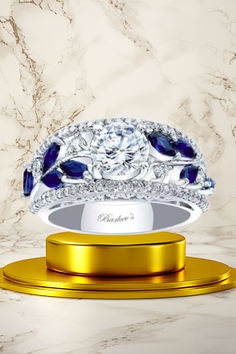 a diamond and blue sapphire ring sits on a gold stand in front of a marble background