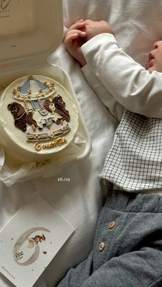 a small child laying on top of a bed next to a box with a cake in it