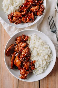 two white bowls filled with chicken and rice on top of a wooden table next to a fork