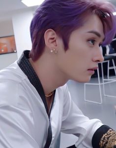 a man with purple hair and tattoos on his arm looking at something in the distance