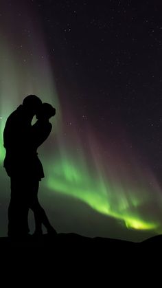 two people are kissing in front of the aurora lights