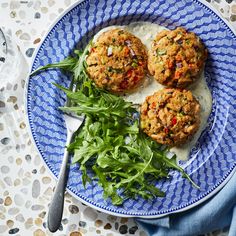 three crab cakes on a blue and white plate next to some green salad leafy greens