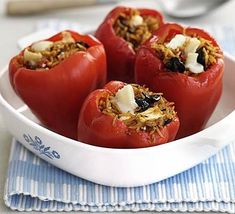 four stuffed tomatoes in a white bowl on a blue and white napkin with spoons