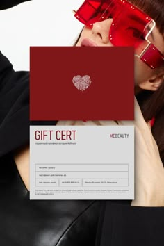 a woman wearing red glasses holding up a gift card with a heart on it's side