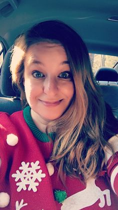 a woman sitting in the back seat of a car wearing a christmas sweater with snowflakes on it