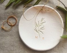 two wedding rings are sitting on a plate next to some flowers and greenery with the initials mr and mrs