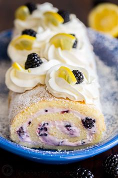 a blue plate topped with a roll covered in whipped cream and berries next to blackberries