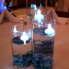 three clear glass vases filled with water and lit candles on top of a table