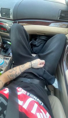 a man with tattoos on his arm laying down in a car wearing a hoodie