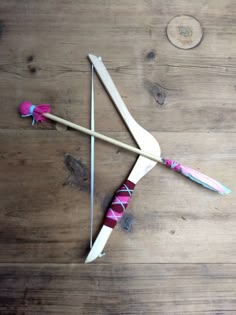 a bow and arrow made out of wood sitting on a wooden floor next to yarn