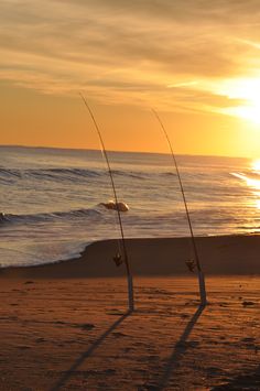 two poles with fishing rods sticking out of them on the beach at sunset or sunrise